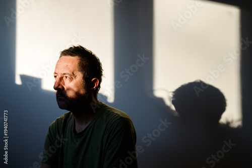 Portrait of bearded middle-aged man with dramatic and intense gaze, deep shadows shaping his face against dark blurred interior.