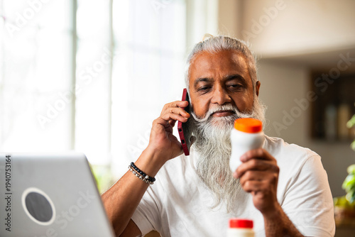 Φωτογραφία Indian man holding pill bottle and verifying medication information on laptop