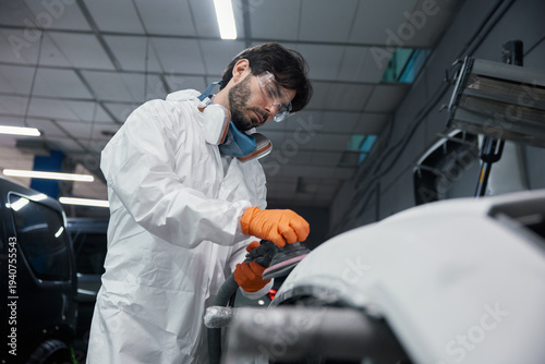 An automotive technician is repairing a car bumper in a workshop while wearing safety gear