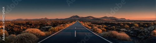 Empty desert road at sunset with mountains in the distance.