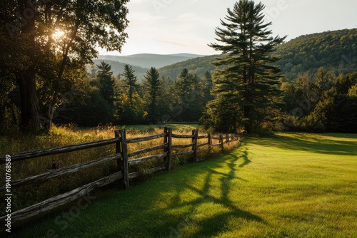 Golden Hour Sunlight Illuminates a Rustic Wooden Fence in a Lush Green Meadow with Distant Mountains.