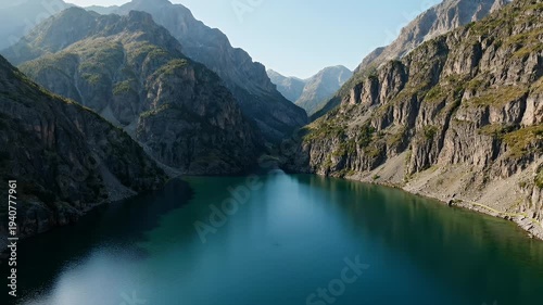 A serene, turquoise lake winds through rugged, sunlit mountain ranges under a clear sky