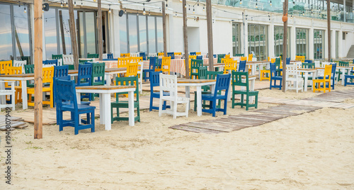 Foto Colorful wooden chairs and tables arranged on a sandy beach terrace of a seaside