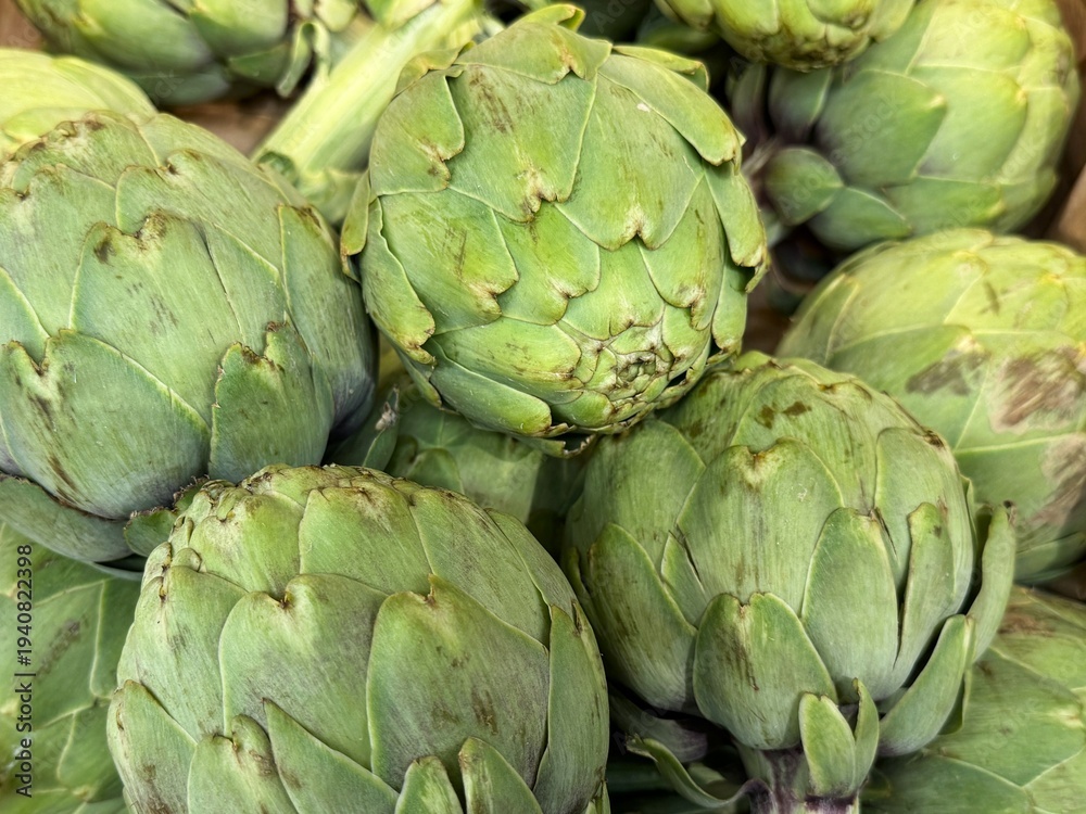 Obraz premium Fresh green artichokes close up at farmers market. Organic seasonal vegetables used in Mediterranean cuisine. Concept of healthy food, fresh produce, plant based diet and natural ingredients.