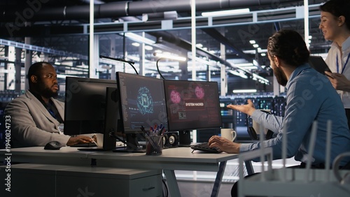 Canvas Print Engineer in server room responding to sudden ransomware detection on monitor, requesting help from manager to protect critical data