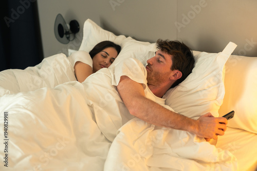 Quadro su tela Upset jealous woman looking at boyfriend’s phone while couple lying in bed at ni