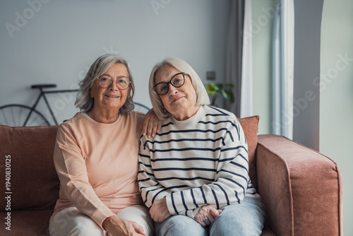 Fotografía Two smiling elderly women sit on a sofa in a cozy living room, enjoying a warm c