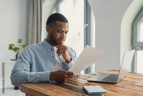 Fotografie Concentrated African American manager reading letter, paper handout, analyzing company statistics, thinking about financial risks, comparing results