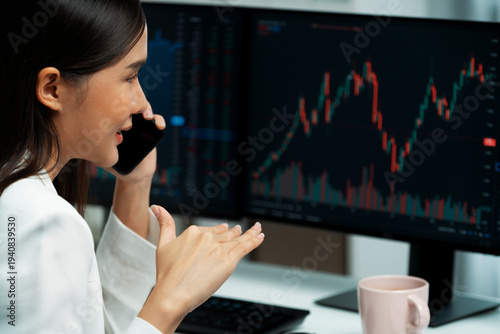 Foto Young beautiful Asian businesswoman calling to broker on phone to analyze stable or higher profit value with profitable each exchange stock market graph on pc screens at modern office