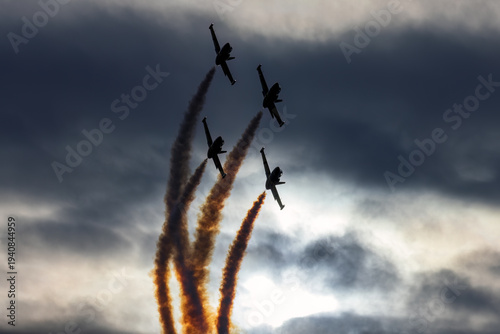 Four L-39 Albatros jet planes perform an aerial display, leaving smoke trails against a dramatic sky.