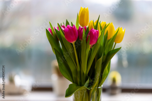 Bouquet of pink and yellow tulips indoors in glass vase on the table