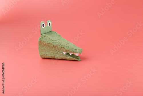 Green crocodile head made from recycled egg carton on pink background. DIY kids craft project for school education, environmental awareness, sustainable toy, creative upcycling hobby, nursery art
