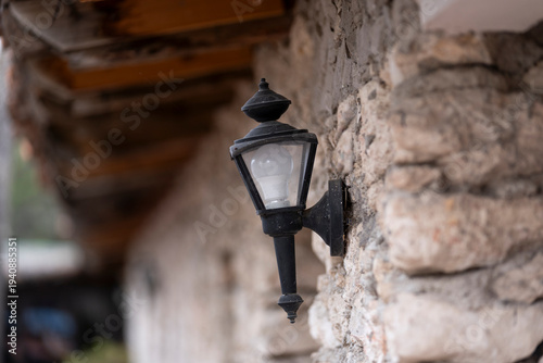 una lámpara rústica negra en el exterior empotrada a la pared de piedra