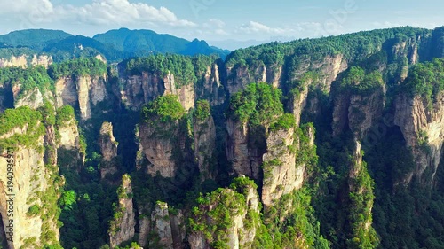 Scenic aerial view of unique quartz-sandstone pillars in Zhangjiajie, Hunan, China, featuring lush green vegetation and breathtaking mountain landscape under blue sky.