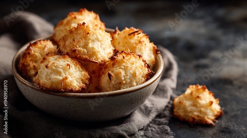 Rustic coconut macaroons in a ceramic bowl with a textured gray cloth, showcasing a delightful confectionary treat with a warm, inviting aesthetic and golden-brown hues.