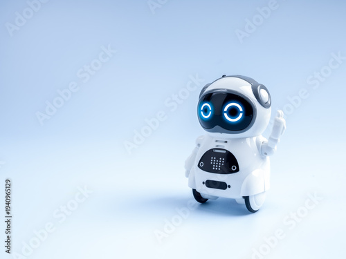 Cute AI robot toy with glowing blue eyes standing with hello raising hand on light background. Friendly chatbot, smart assistant, artificial intelligence, and futuristic automation technology concept.