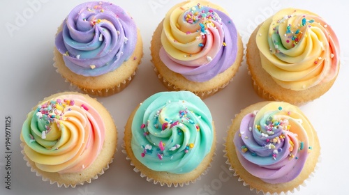 A delightful top-down composition of vanilla cupcakes with pastel swirl frosting and colorful sprinkles, arranged on a white surface, showcasing sweet indulgence