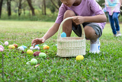The children are having fun on an Easter egg hunt in the lawn. Two little girl bent down to pick up the Easter eggs and put them in their baskets. Children and Easter.