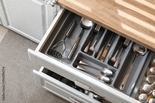 Foto Open kitchen drawer with different silver cutlery and set of spices, top view
