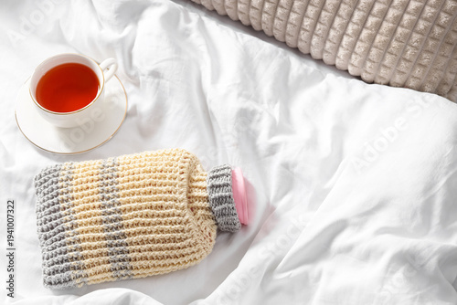 Photography Pink hot water bottle with cup of tea on bed in bedroom, top view