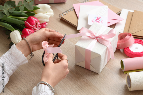 Woman with tulip flowers and packing materials cutting ribbon on gift box at ...