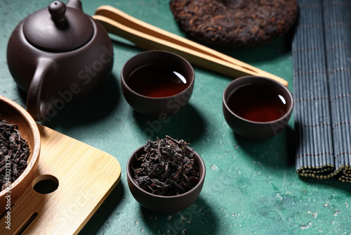 Photos Teapot with cups of hot black tea and dry leaves on grunge turquoise background