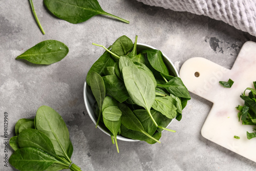 Bowl with fresh spinach leaves and board on grey grunge background