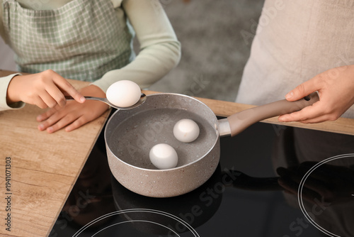 Tableau sur toile Little girl with her mother boiling eggs in kitchen, closeup