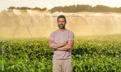 Mature man at irrigation system watering agricultural field. Farmer man in countryside. Water sprinkler irrigating crop field. Drip irrigation system. Crop irrigation. Agriculture and farming
