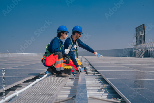 Slika na platnu Solar technicians kneel beside photovoltaic panels on industrial rooftop while checking wiring and panel alignment