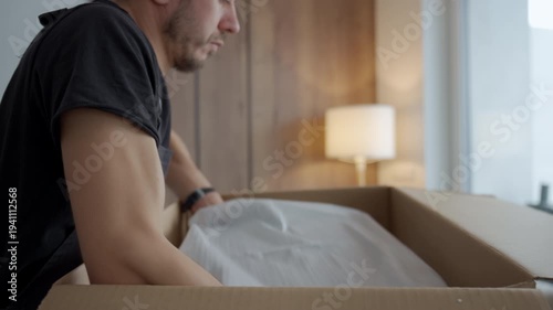 Person removes appliance covered in protective fabric from open cardboard box. Concept of appliance installation preparation and product unboxing process.
