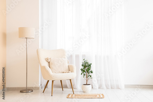 Interior of light living room with white armchair, floor lamp and houseplant near big window