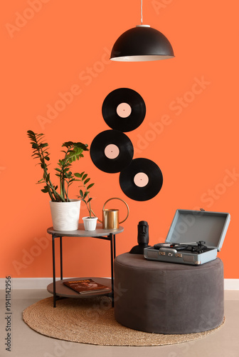 Table, pouf, record player and houseplants near orange wall in room