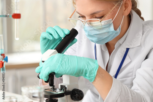 Female scientist with medical mask and microscope working in laboratory, closeup