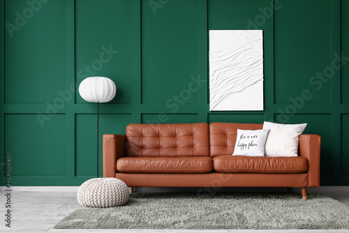 Brown leather sofa with soft pillows and floor lamp near green wall in living room