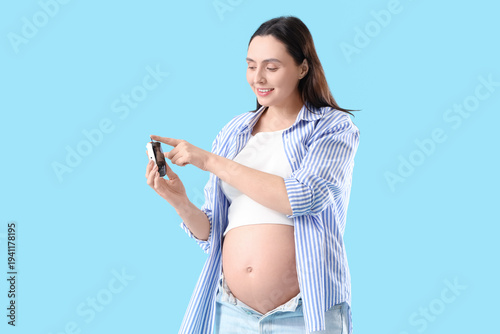Foto Young pregnant woman using glucometer on blue background