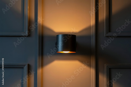 A contemporary black wall sconce casts a warm downward glow on a textured gray paneled wall.