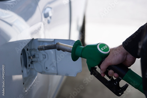 Tablou pe pânză man refilling car with e20 biofuel at gas station, hand holding green fuel nozzl