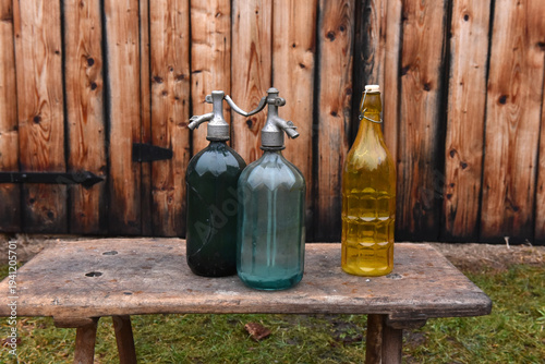 Konstfotografi Vintage glass soda siphons and yellow bottle on rustic wooden bench