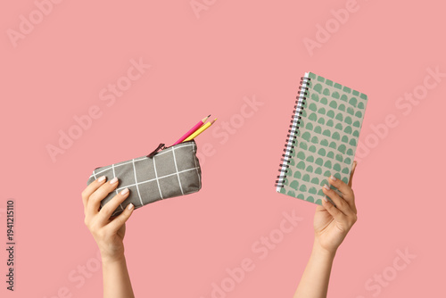 Obraz na plátně Female hands holding notebook and pencil case with stationery on pink background