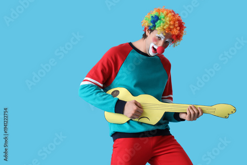 Portrait of clown playing toy guitar on blue background. April Fool's day cel...