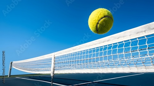 Tennis ball flying over net on court against clear blue sky during match, outdoor view