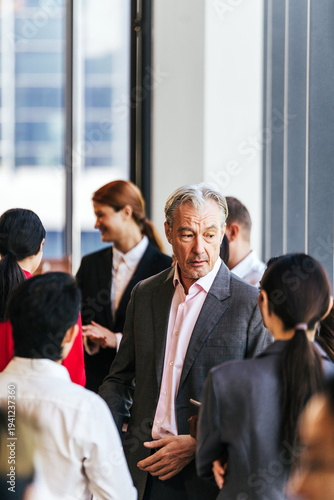 Professionals in suits network and converse at a corporate event near large windows in a modern office building.