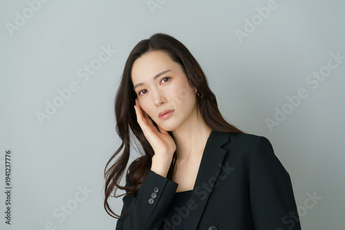 グレーバックの悩める黒いスーツを着た若い日本人女性のポートレート