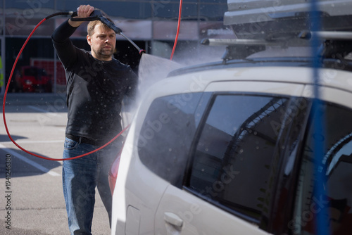 Obraz na plátne man washing white car with high pressure water jet at self service station using