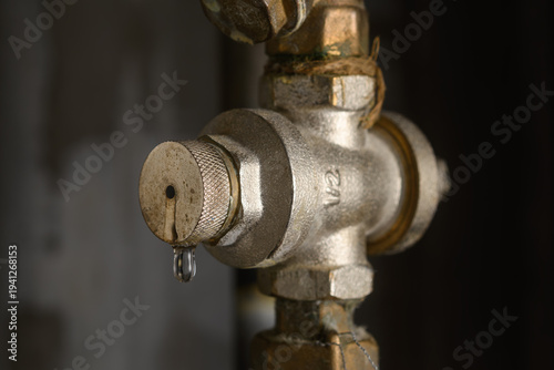 фотографія Leaking water pressure regulator on metal pipe in dark utility room signals home plumbing fault and need for urgent service