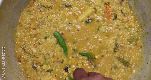 south Asian rice lentils khichuri khichdi soft runny porridge with diced vegetable boiling sizzling in a pot over flame top flatly view 