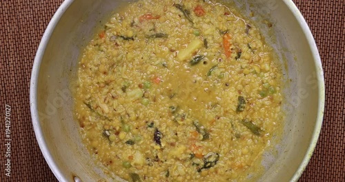 south Asian rice lentils khichuri khichdi soft runny porridge with diced vegetable boiling sizzling in a pot over flame top flatly view 