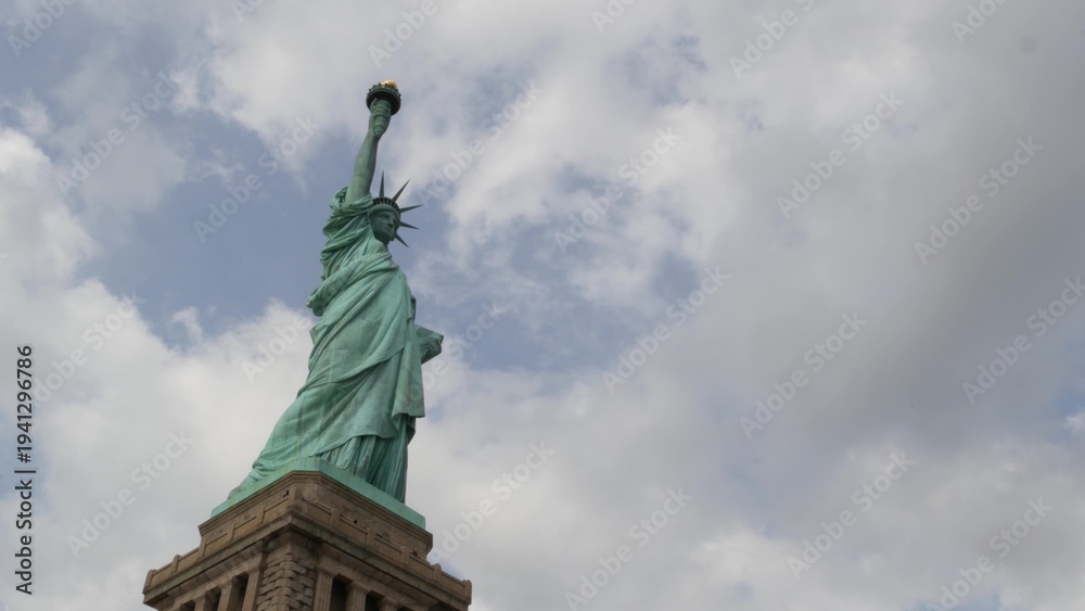 Fototapeta premium Statue of Liberty on Liberty Island, New York, United States. Blue cooper monument, symbol of democracy and patriotism near Manhattan, NYC USA. Clouds on sky. American independence. Torch and crown.