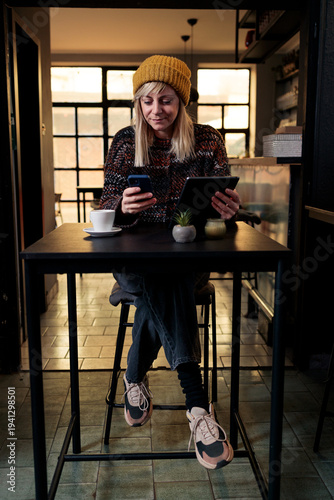 Woman multitasking using phone and digital tablet in cafe